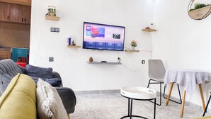 Una sala moderna con un televisor de pantalla plana montado en la pared, un sofá, una mesita redonda y una silla.