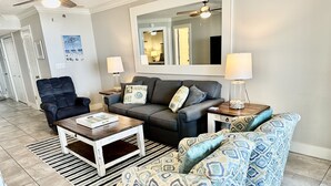 Una sala de estar con un sofá gris, un sillón azul, una mesa de centro de madera y un sofá estampado.