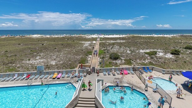 Un resort con varias piscinas, un paseo marítimo que conduce a la playa y sombrillas de playa.