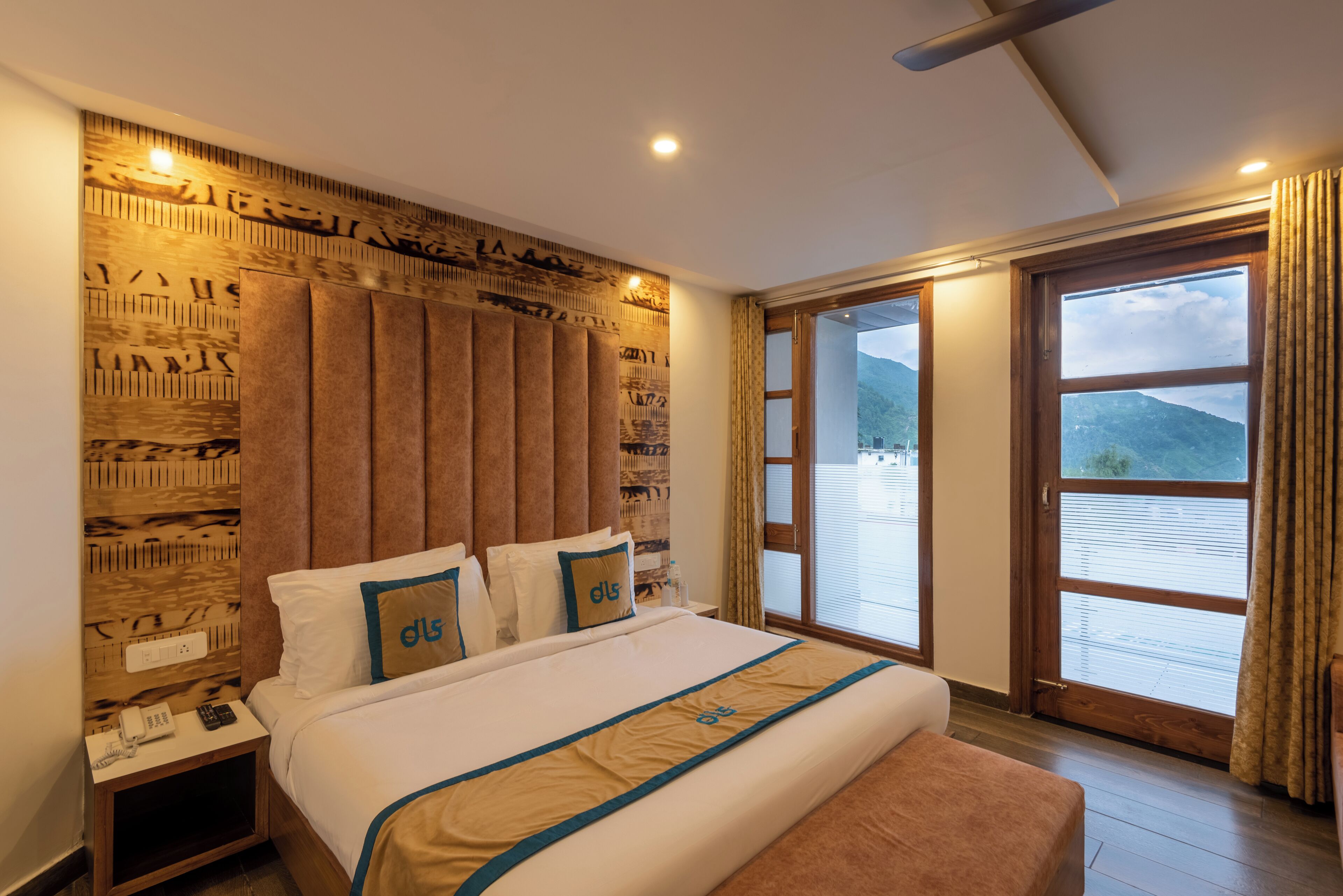 Ein Hotelzimmer mit einem großen Bett, einem Holzkopfende und Bergblick aus den Fenstern.