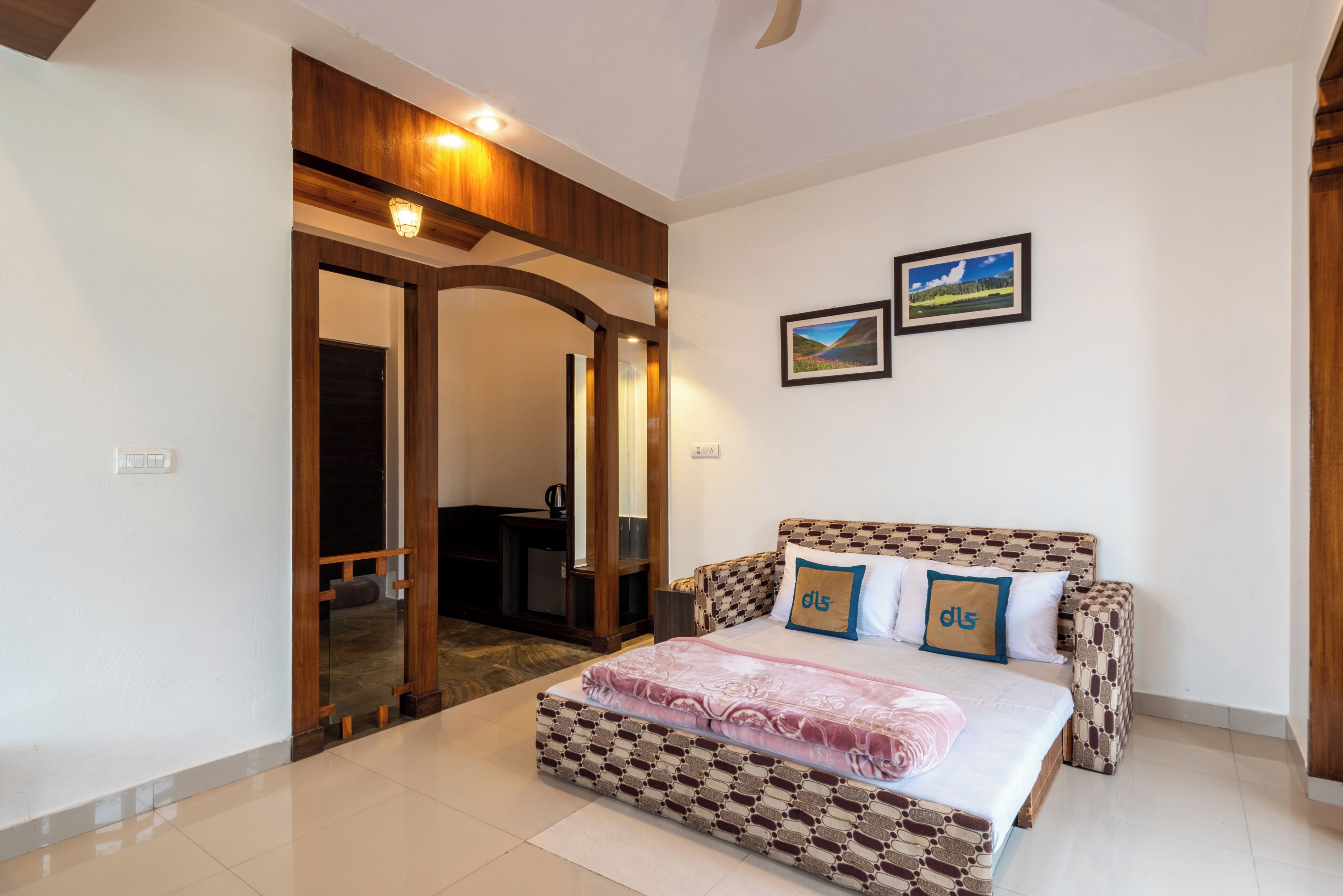 A bedroom with a patterned bed, a wooden door, and two framed pictures on the wall.