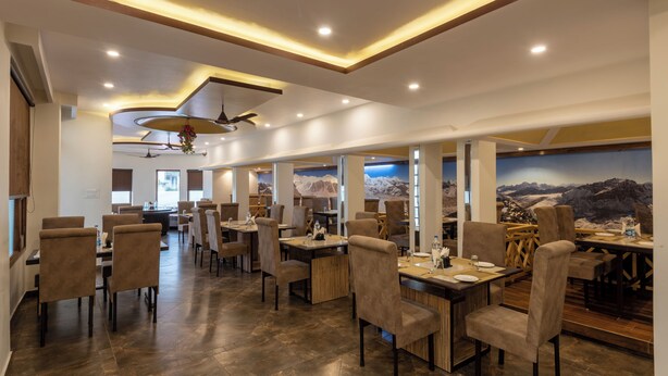 A modern restaurant with a high ceiling, recessed lighting, and a mural of a mountainous landscape. - Meghavan Resort By DLS Hotels (Dharamshala)