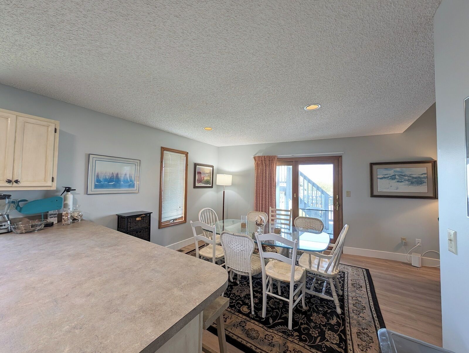 A kitchen with a large island, dining area with chairs, a window with blinds, and a door leading outside.