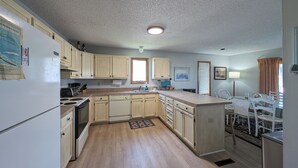 A compact kitchen with wooden cabinets, a refrigerator, a sink, and a dining area with chairs. - 5 Bedroom Dog Friendly House with community pool and beach views! (Fenwick Island)