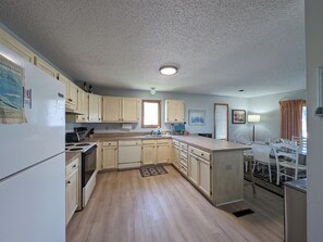 A compact kitchen with wooden cabinets, a refrigerator, a sink, and a dining area with chairs. - 5 Bedroom Dog Friendly House with community pool and beach views! (Fenwick Island)