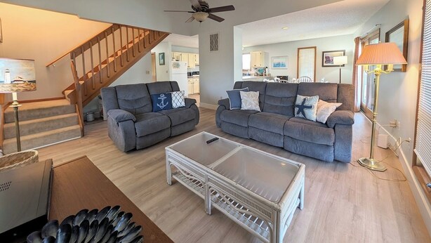 A living room with two grey sofas, a white coffee table, a wooden staircase, and a ceiling fan. - 5 Bedroom Dog Friendly House with community pool and beach views! (Fenwick Island)