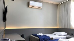 Habitación de hotel con dos camas, un escritorio, una silla, aire acondicionado y televisor montado en la pared.