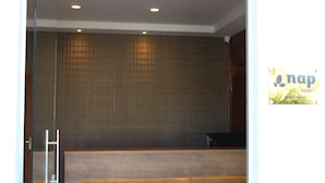 Zona de recepción con un mostrador de madera, una puerta de vidrio y una pared con diseño de cuadrícula.