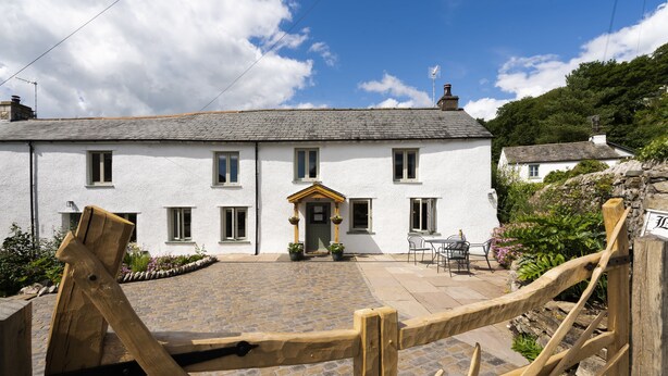 A white building with a stone-paved courtyard, a wooden gate, and a small outdoor seating area. - Joe's Cottage -  Modern, yet cosy, two bedroom cottage - Brigsteer (Brigsteer)