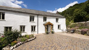 A white building with a stone-paved courtyard, a wooden door, and a stone wall with flowers. - Joe's Cottage -  Modern, yet cosy, two bedroom cottage - Brigsteer (Brigsteer)