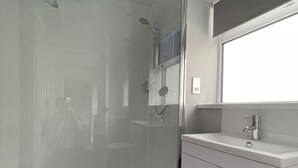 A modern bathroom with a glass shower enclosure, a sink with a mirror, and a dark floor.