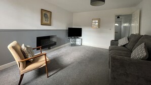 A living room with a flat-screen TV, a sofa, a chair, and a fireplace.