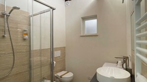 Ein modernes Badezimmer mit Duschkabine aus Glas, einem weißen Waschbecken und einer Toilette.