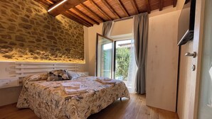 Ein Schlafzimmer mit Steinsandsteinwand, Holzboden und einem Bett mit floralem Bettzeug, mit Blick auf Grünfläche.