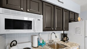 A kitchen with a microwave, kettle, sink, and a coffee maker. - Steps to Beach Access | Updated Condo | Pool | Sleeps 4 (Madeira Beach)