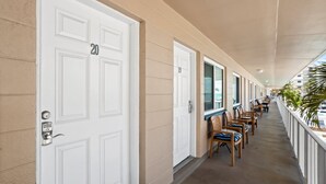 A hotel corridor with white doors, numbered 20, and a row of wooden chairs with blue cushions. - Steps to Beach Access | Updated Condo | Pool | Sleeps 4 (Madeira Beach)