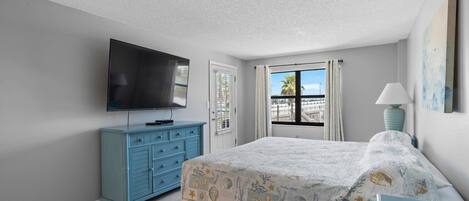 A bedroom with a bed, a TV, a dresser, a window with curtains, and a lamp.