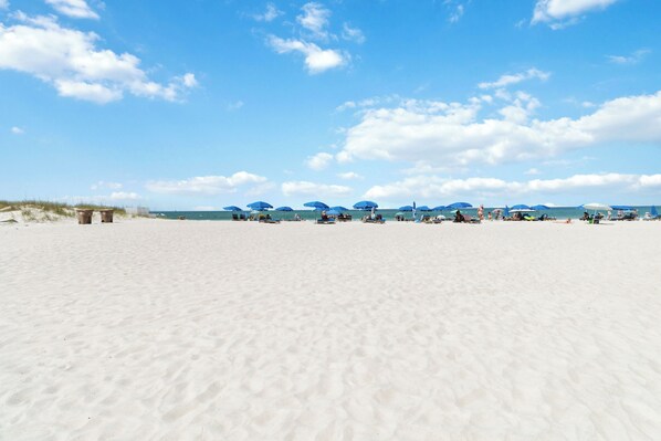 A wide sandy beach with several blue umbrellas and a few people.
