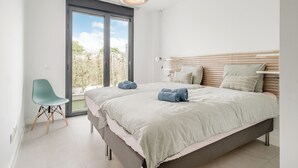 Ein modernes Schlafzimmer mit einem großen Bett, einem Sessel und Blick ins Grüne durch eine Schiebetür.