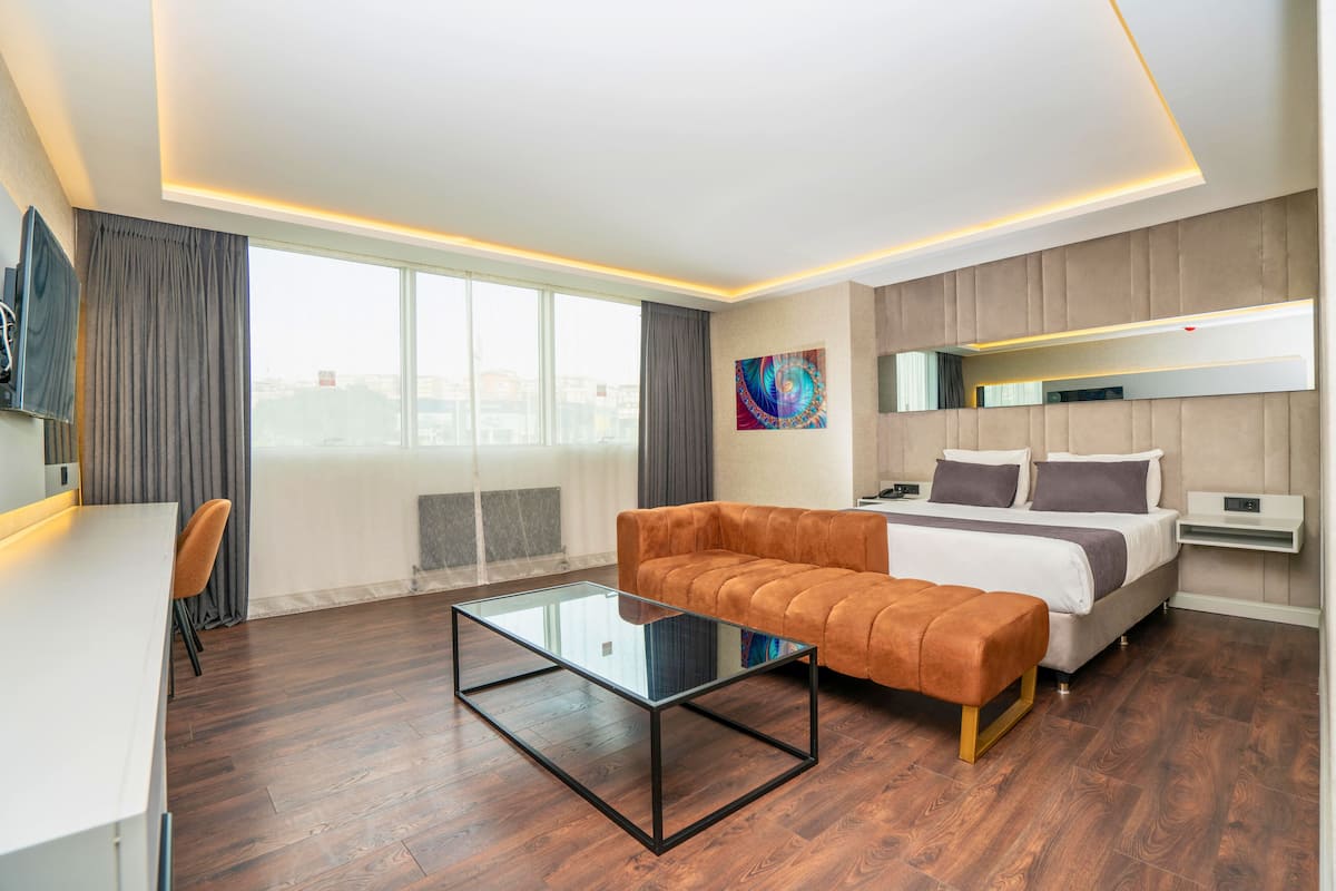 Ein modernes Hotelzimmer mit einer Couch, einem Glastisch, einem Bett mit Kopfteil, einem Fernseher und Blick auf die Stadt.