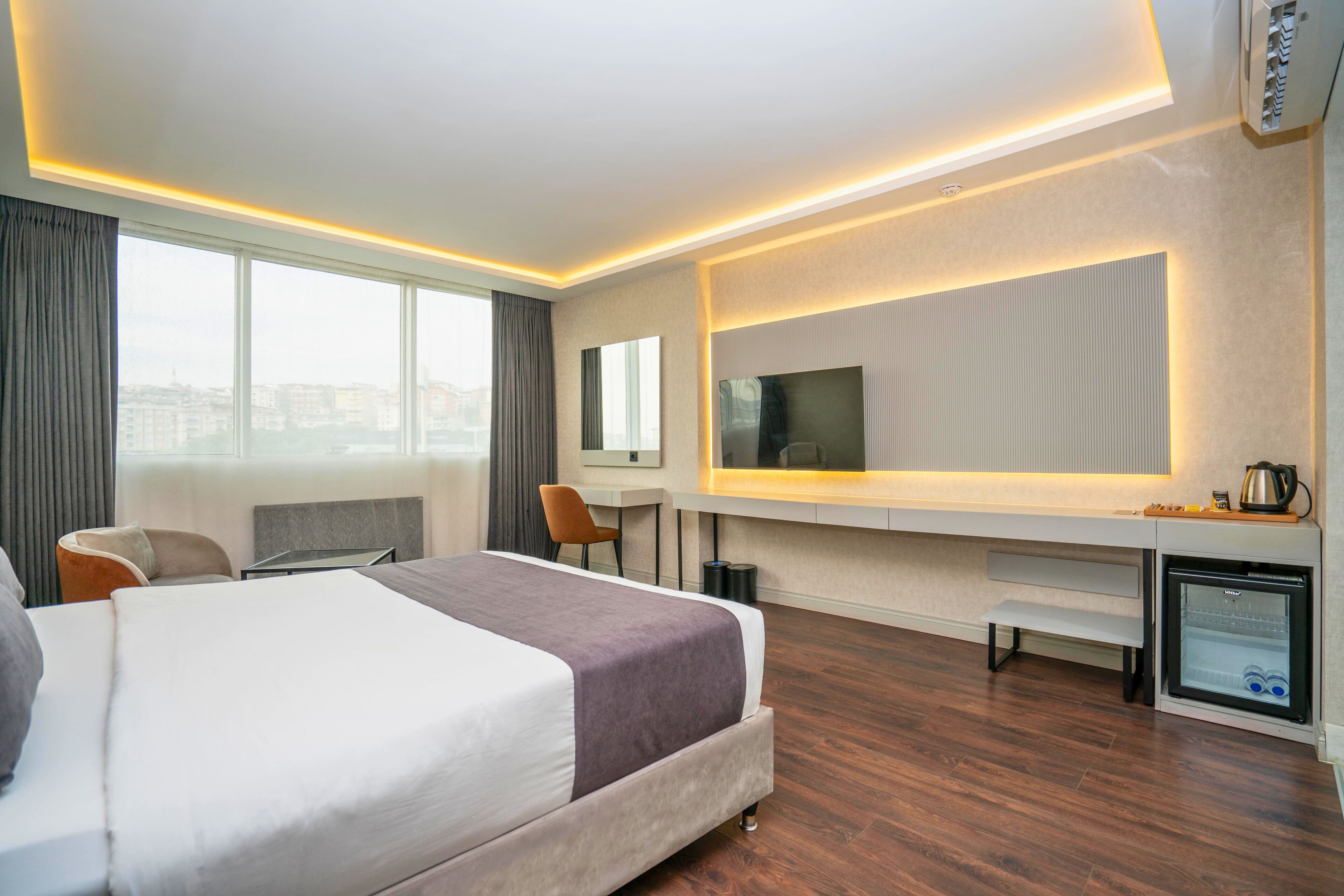 Moderni hotellihuone, jossa on suuri sänky, työpöytä, tuoli, televisio ja minibaari.