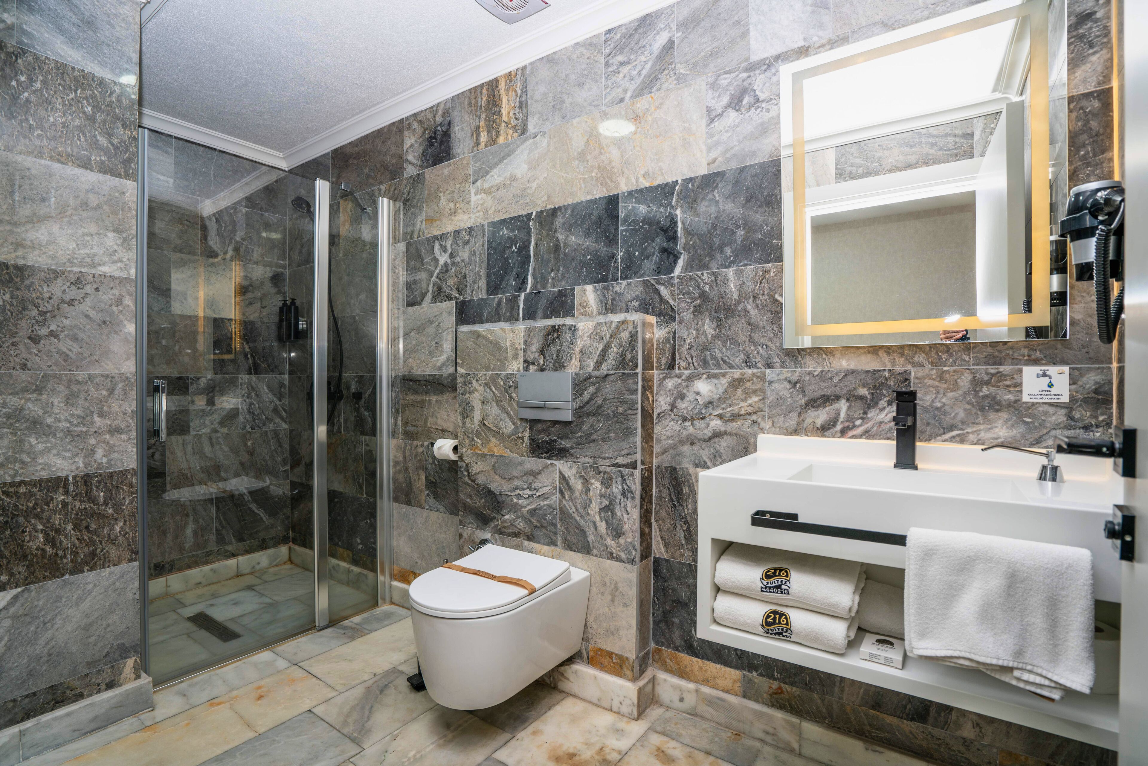Un baño moderno con ducha envuelta en vidrio, inodoro blanco y tocador con espejo y toallero.