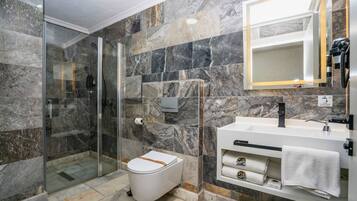 Un baño moderno con ducha envuelta en vidrio, inodoro blanco y tocador con espejo y toallero.