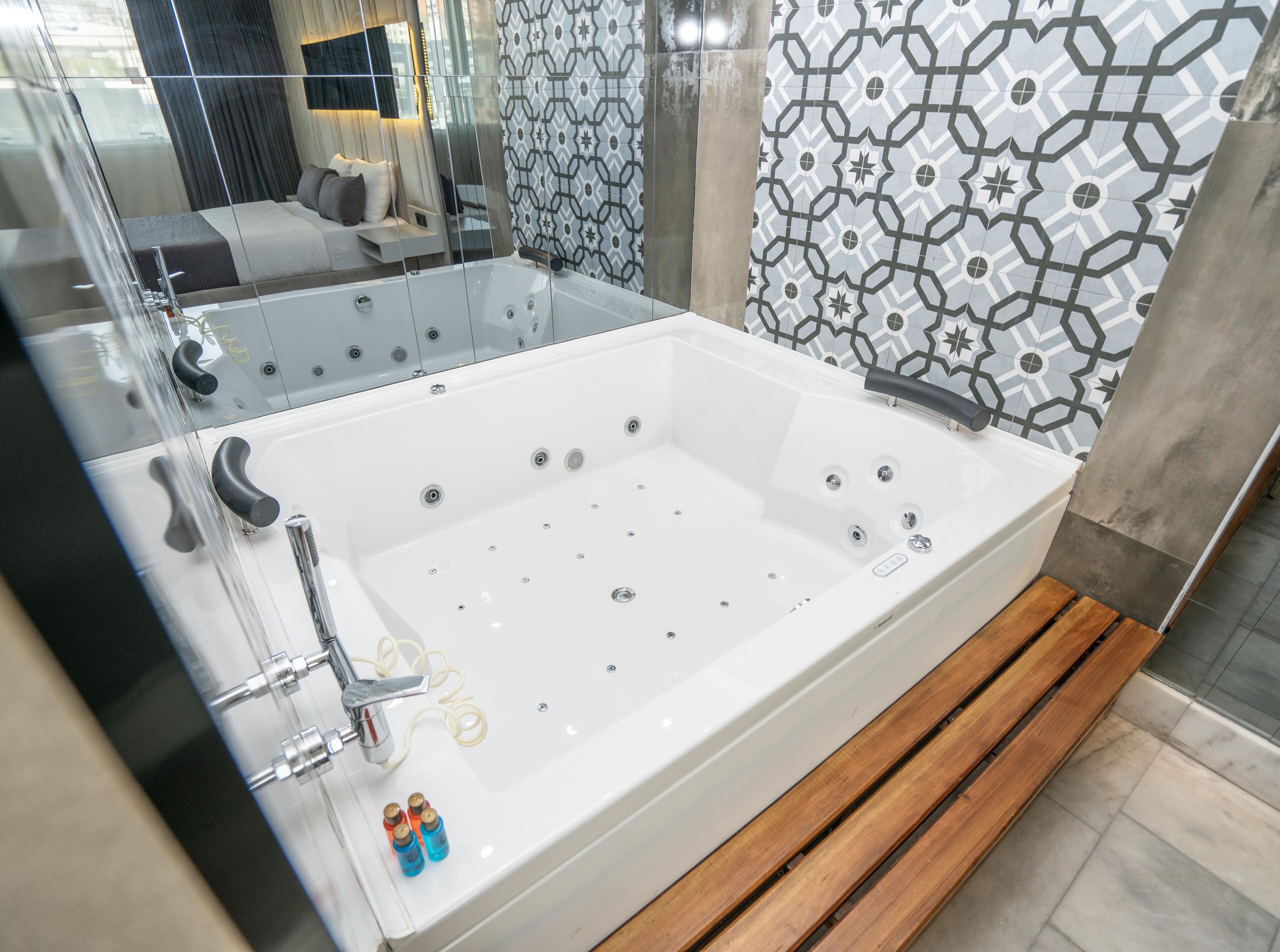 A modern bathroom with a large white bathtub, a glass-enclosed shower area, and a patterned tile wall.