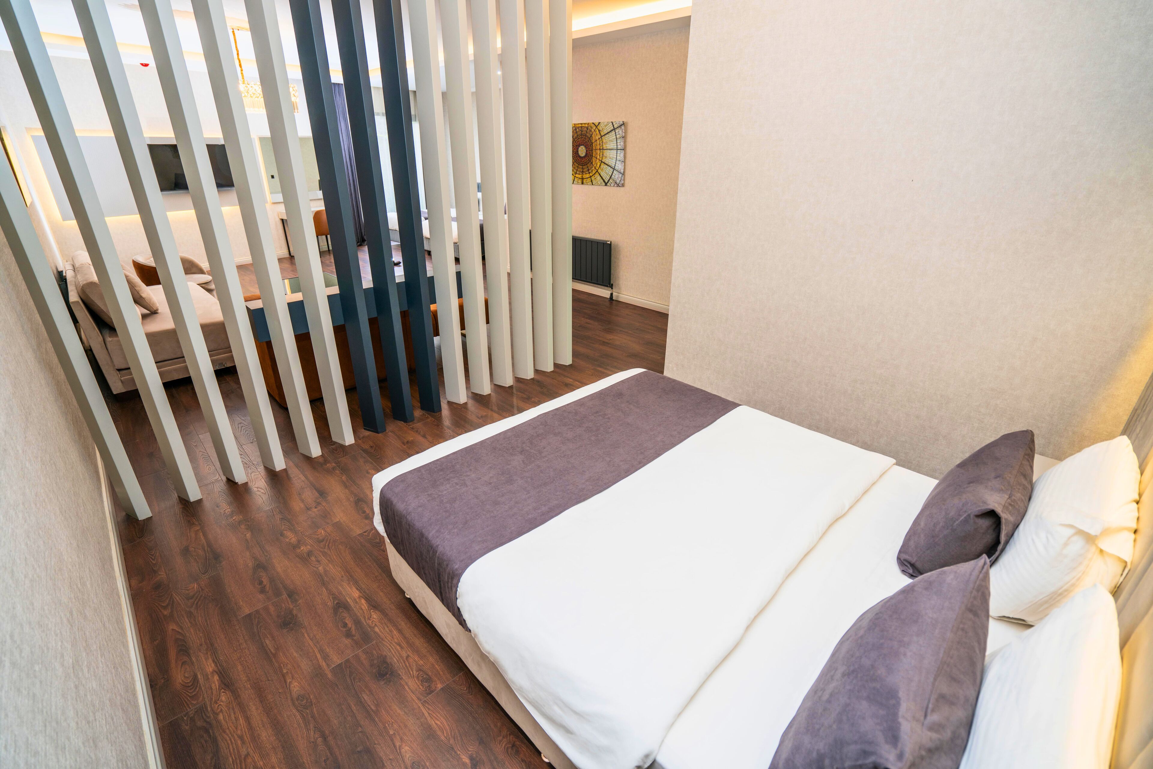 A bedroom with a bed, white curtains, and a wooden floor.