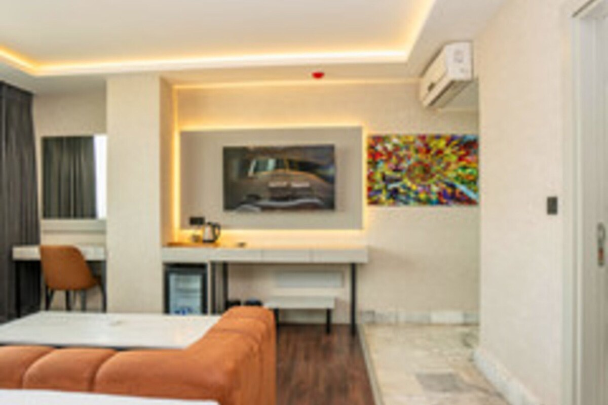 Una habitación de hotel moderna con una cama, un escritorio y una silla. Hay un cuadro en la pared y un equipo de aire acondicionado.
