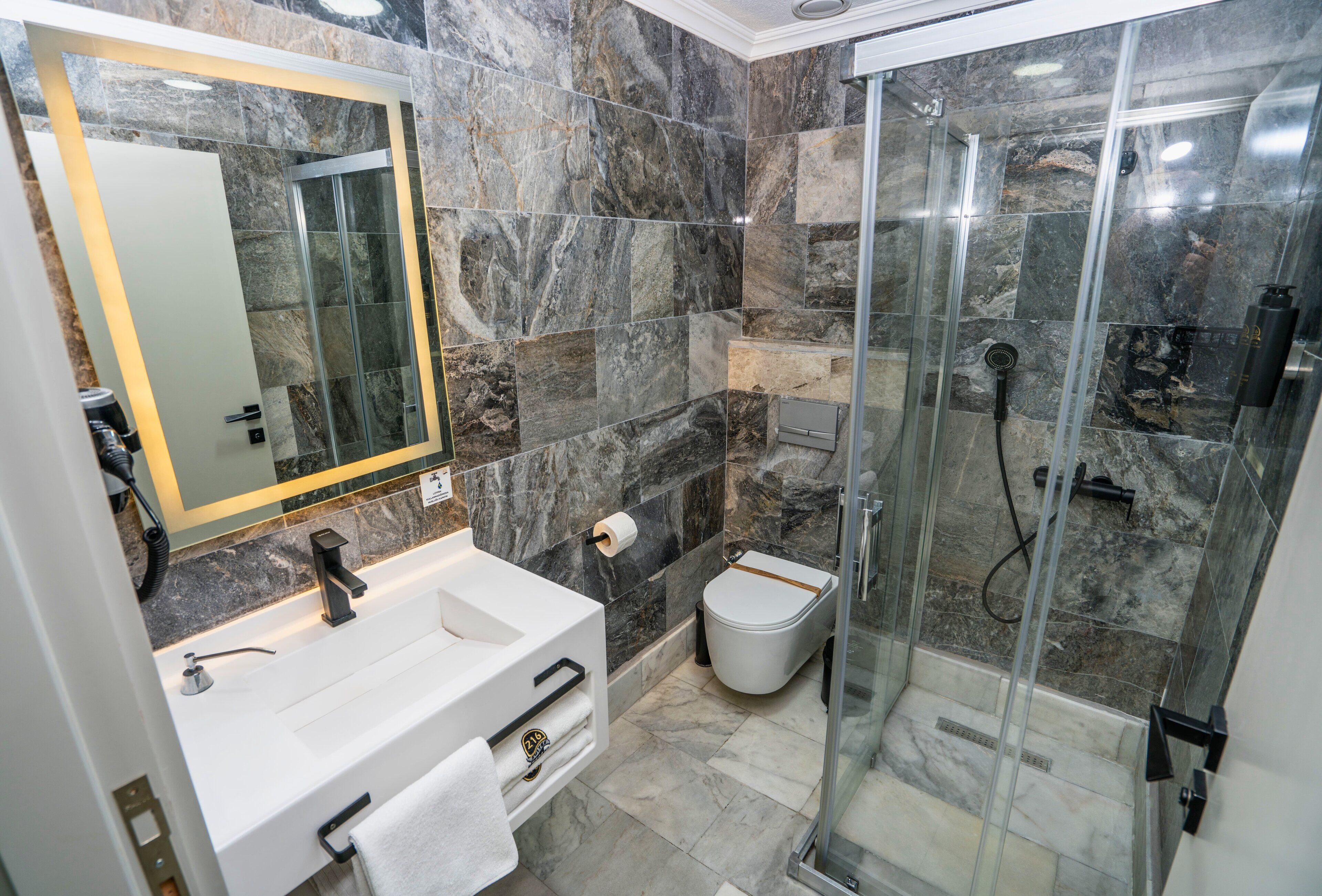 A modern bathroom with a marble shower, a white sink, and a toilet.