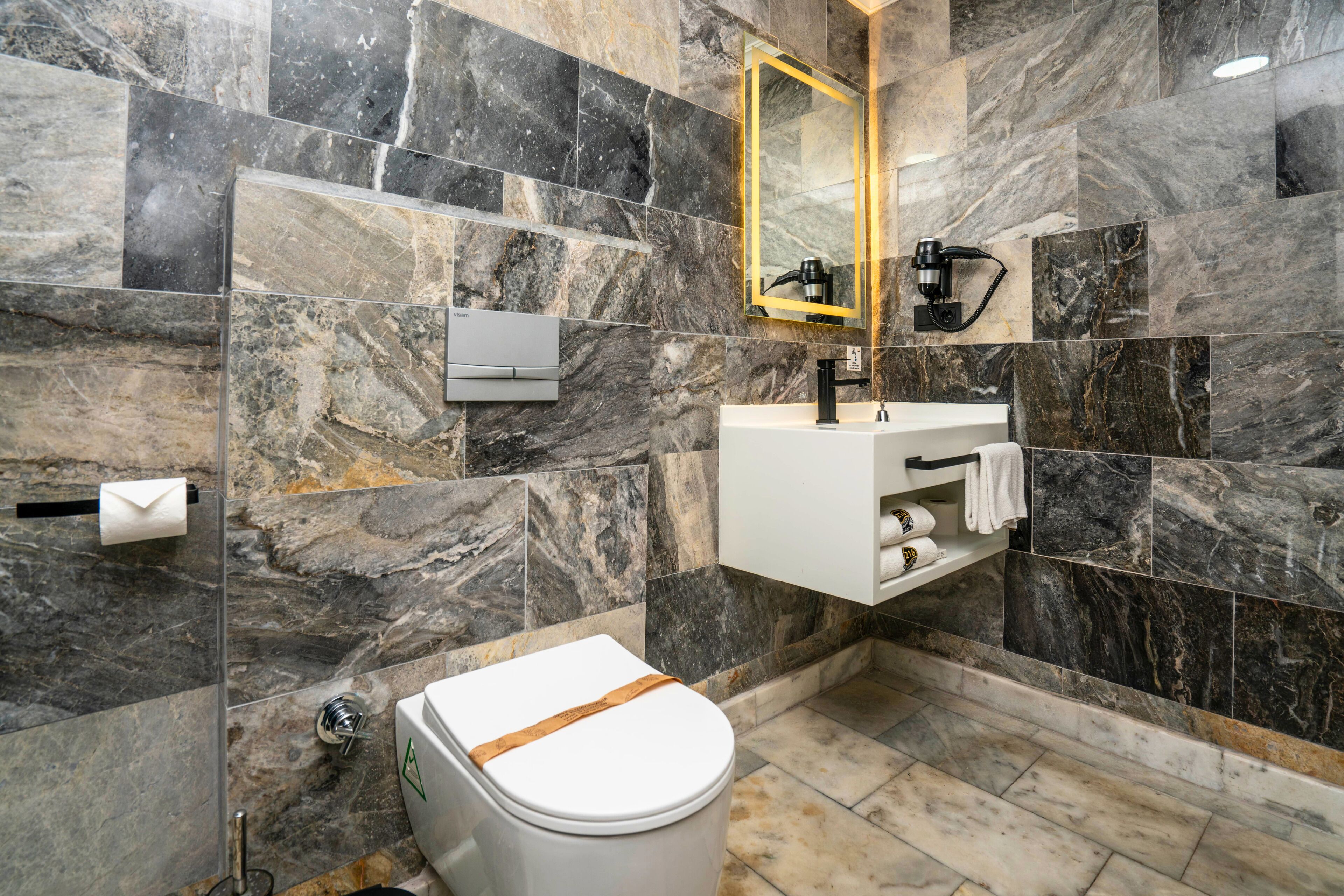 A modern bathroom with a marble wall, a white sink, and a toilet.