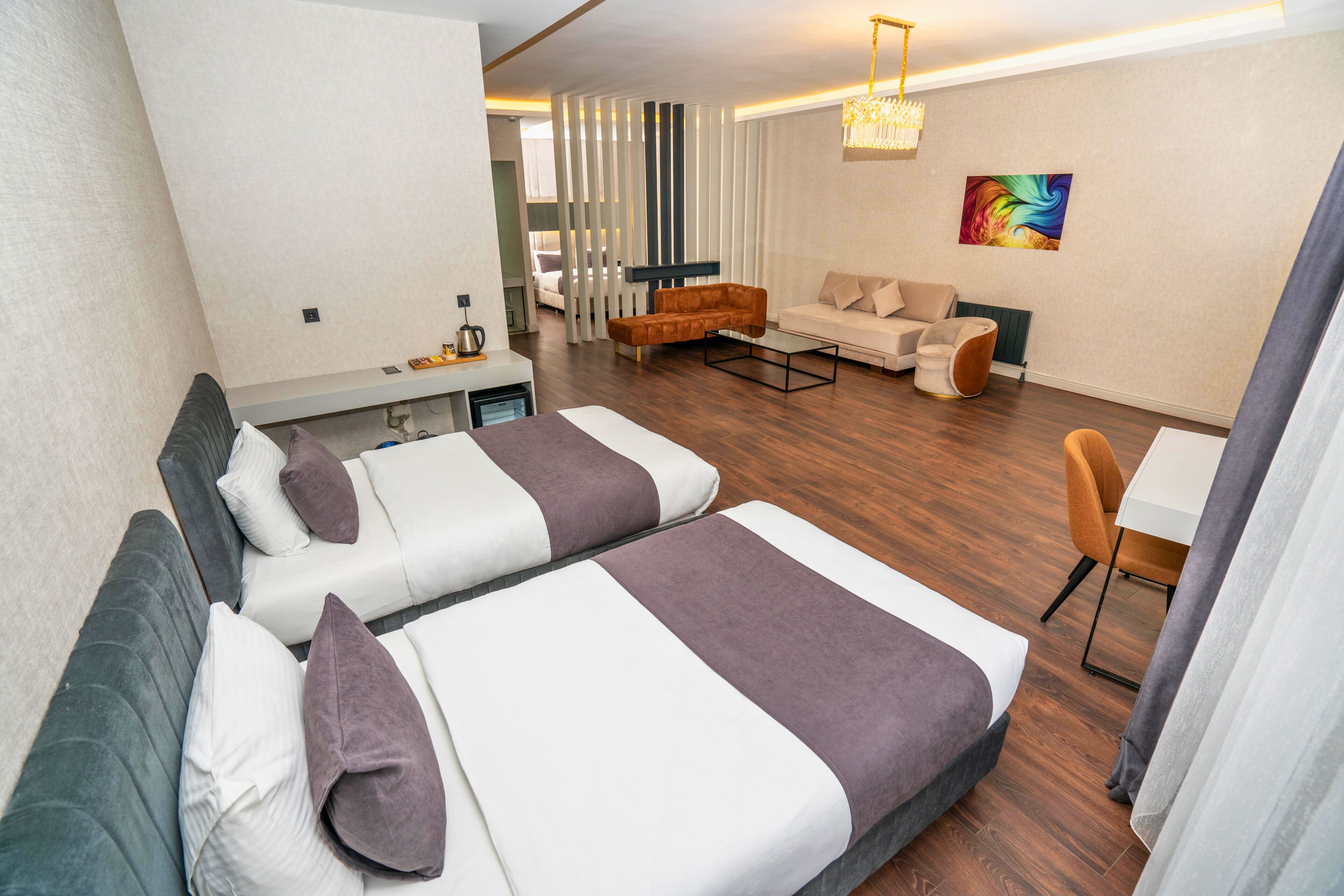 A modern hotel room with two beds, a sofa, a dining table, and a colorful abstract painting on the wall.