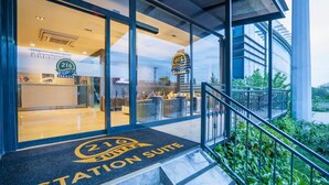 Entrada de hotel com design moderno, área de recepção visível e escadaria que leva ao acesso.
