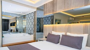 Quarto de hotel moderno com uma cama grande, uma banheira embutida e um espelho amplo que reflete o ambiente.
