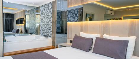 A modern hotel room with a large bed, a built-in bathtub, and a large mirror reflecting the room.