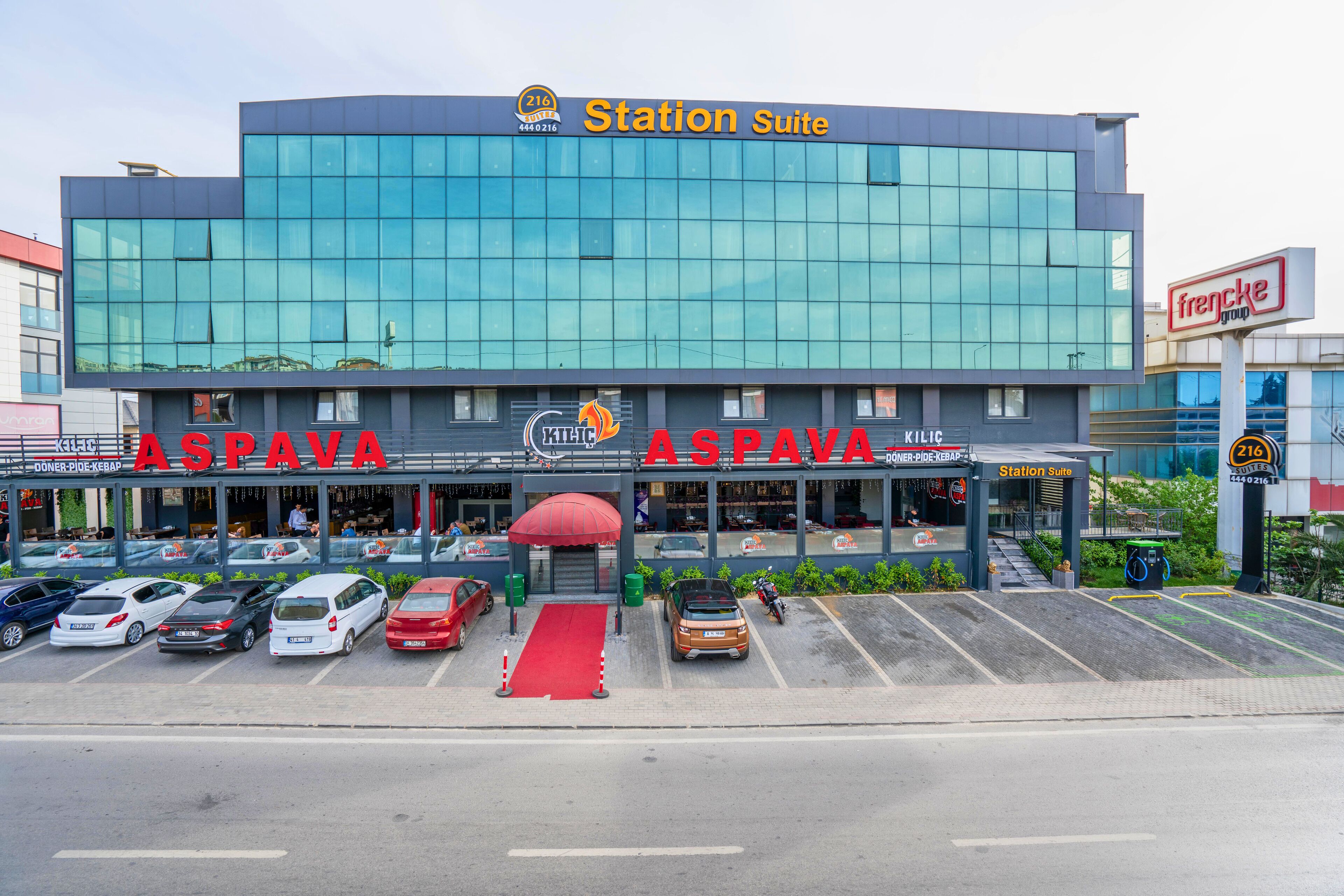 A modern building with a glass facade, a red carpet entrance, and multiple parking spaces.