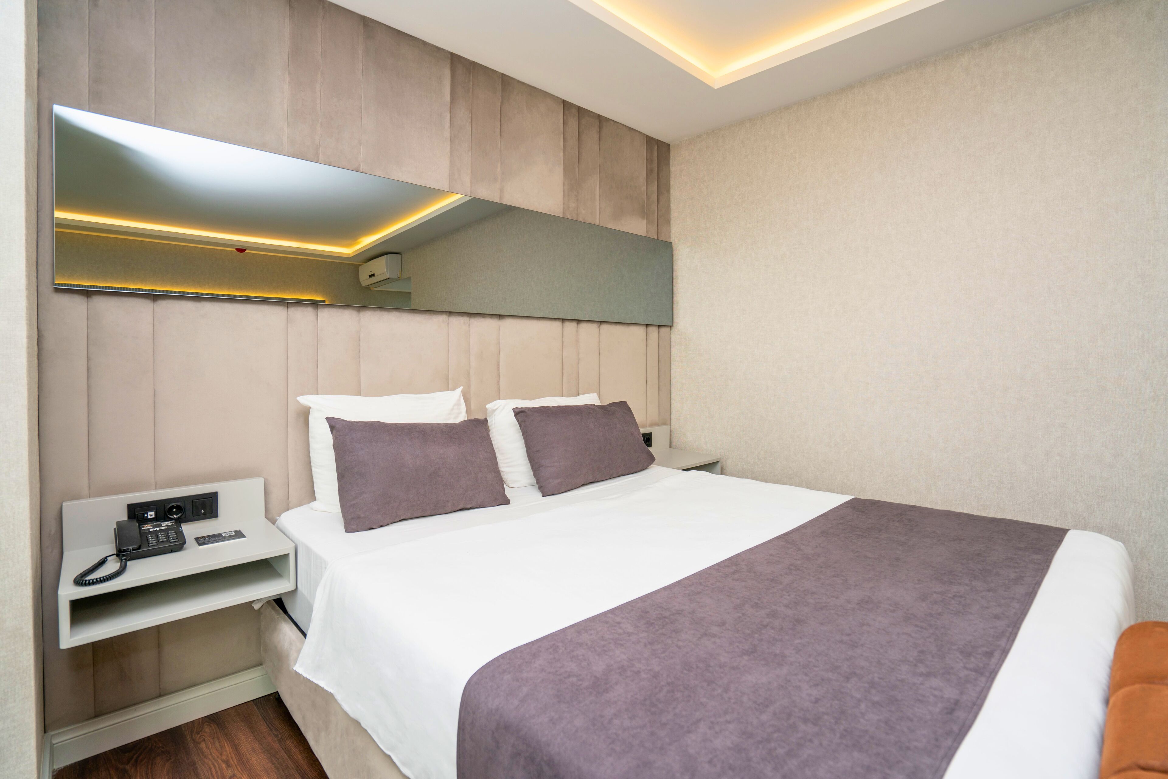 Una habitación de hotel con una cama, una mesita de noche con un teléfono, una lámpara auxiliar y un espejo montado en la pared.
