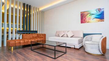 A modern living room with a sofa, a coffee table, and a chair. There is a decorative wall panel and a painting on the wall.