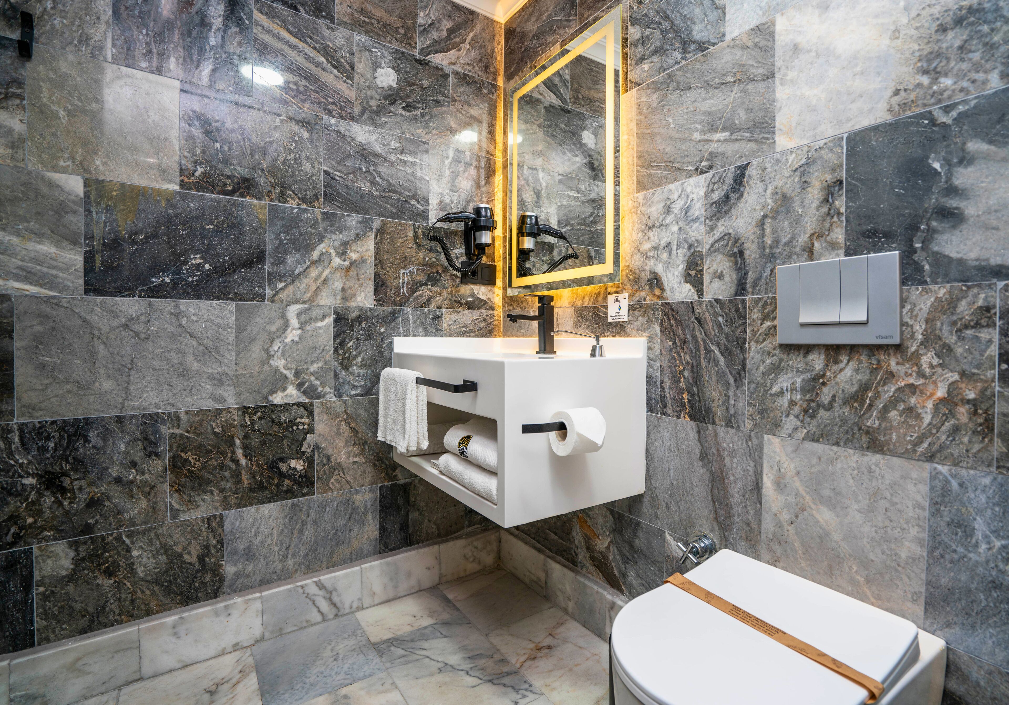 A bathroom with a marble wall, a white sink with a mirror, and a toilet.