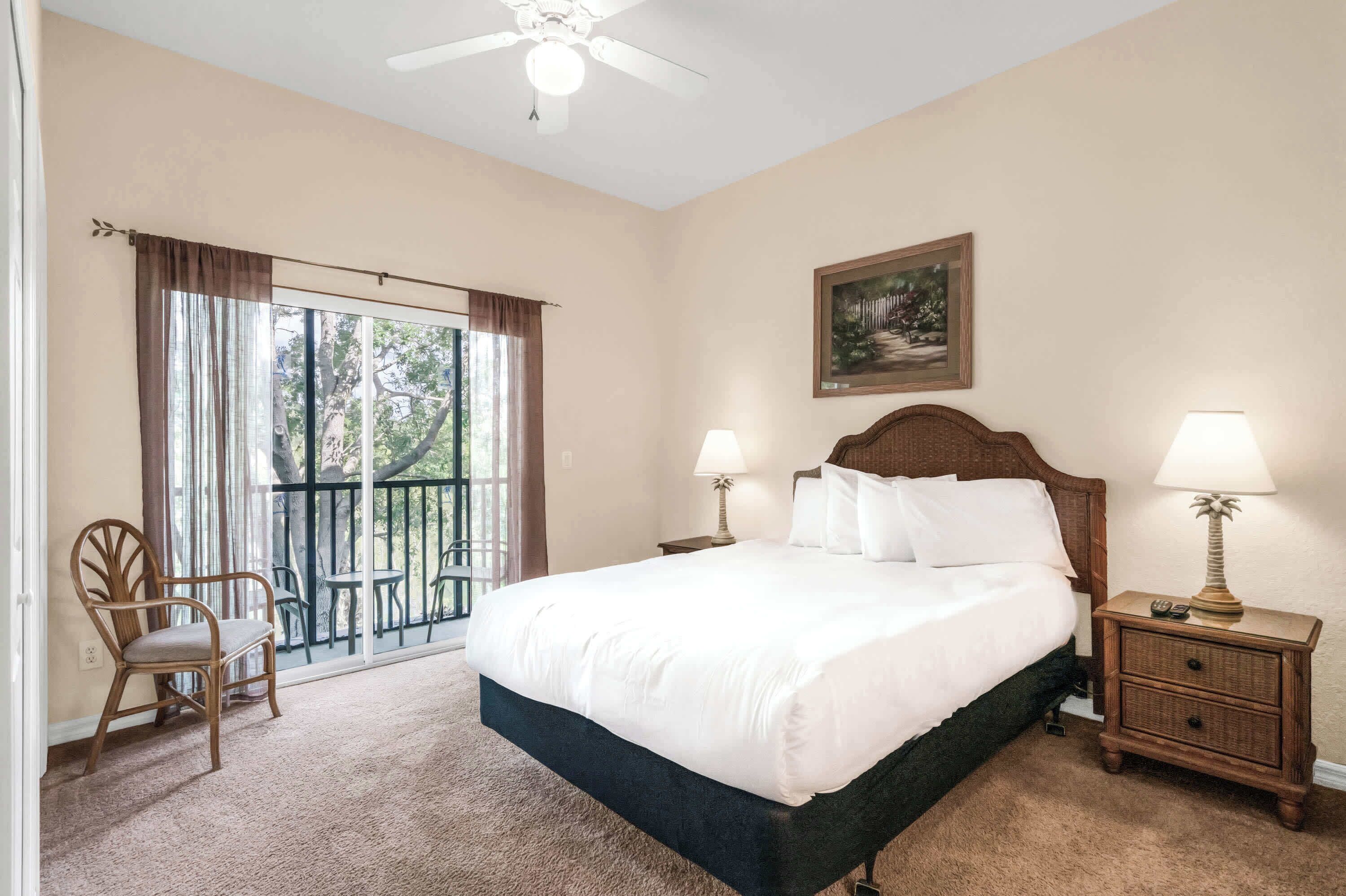 Une chambre dotée d’un grand lit, de deux tables de chevet avec des lampes, d’une chaise, d’un balcon avec vue et d’un ventilateur de plafond.