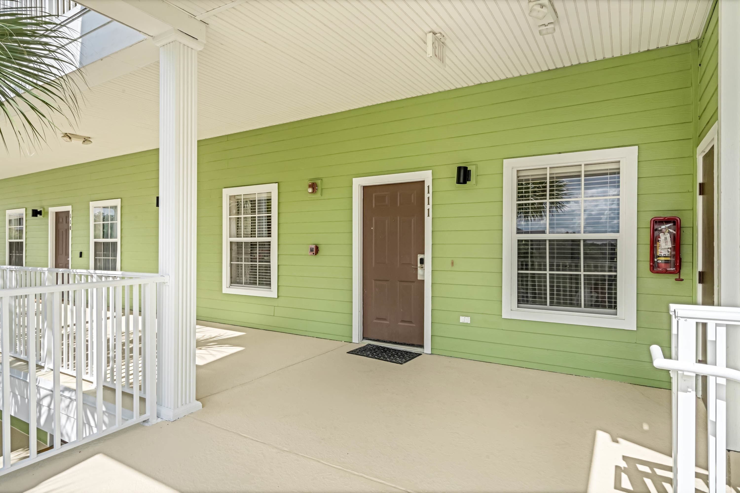 A green building with white railings, a brown door, and a window with a metal grill.