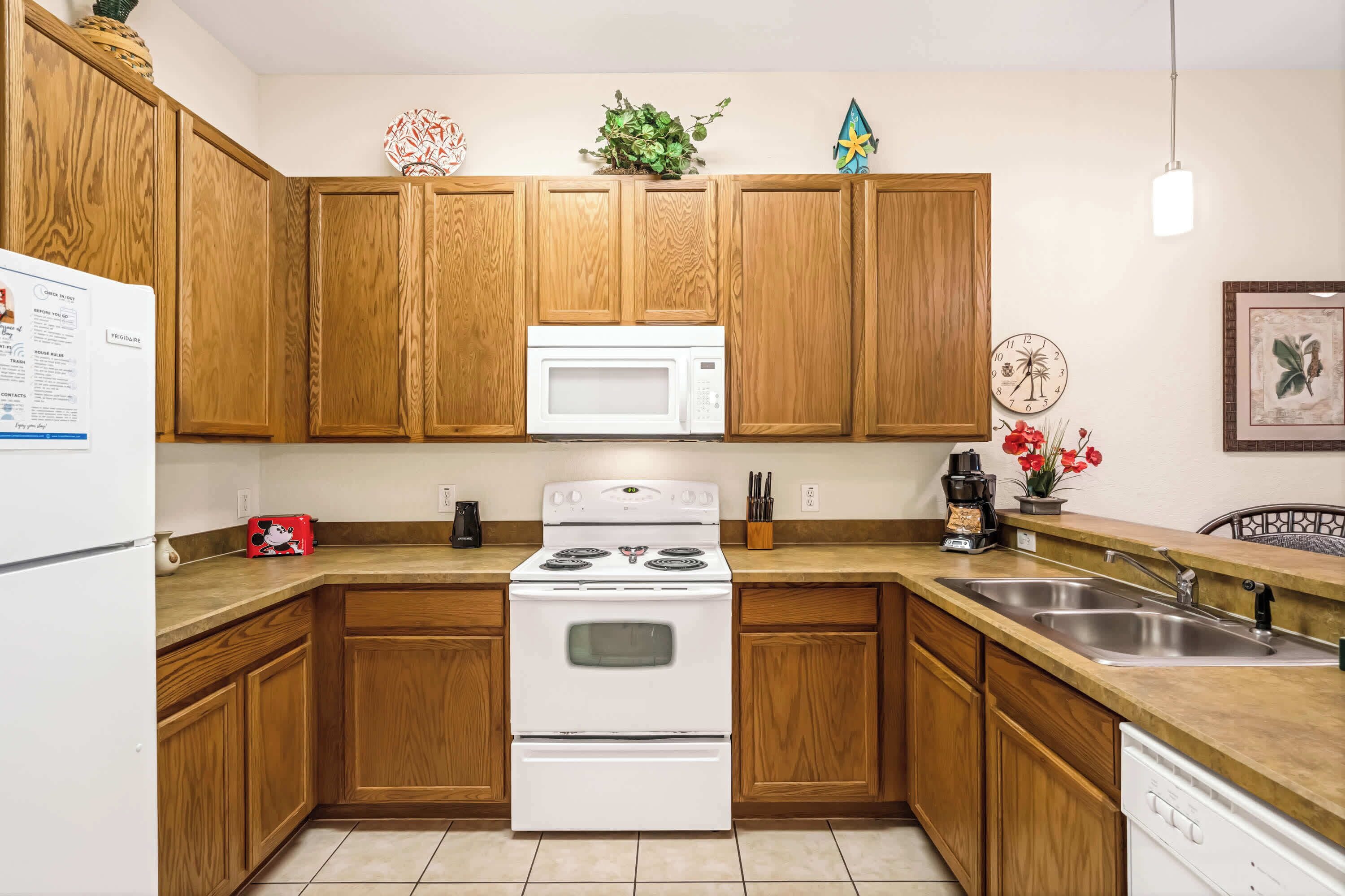 A kitchen with wooden cabinets, a white stove, a microwave, a sink, and a refrigerator.