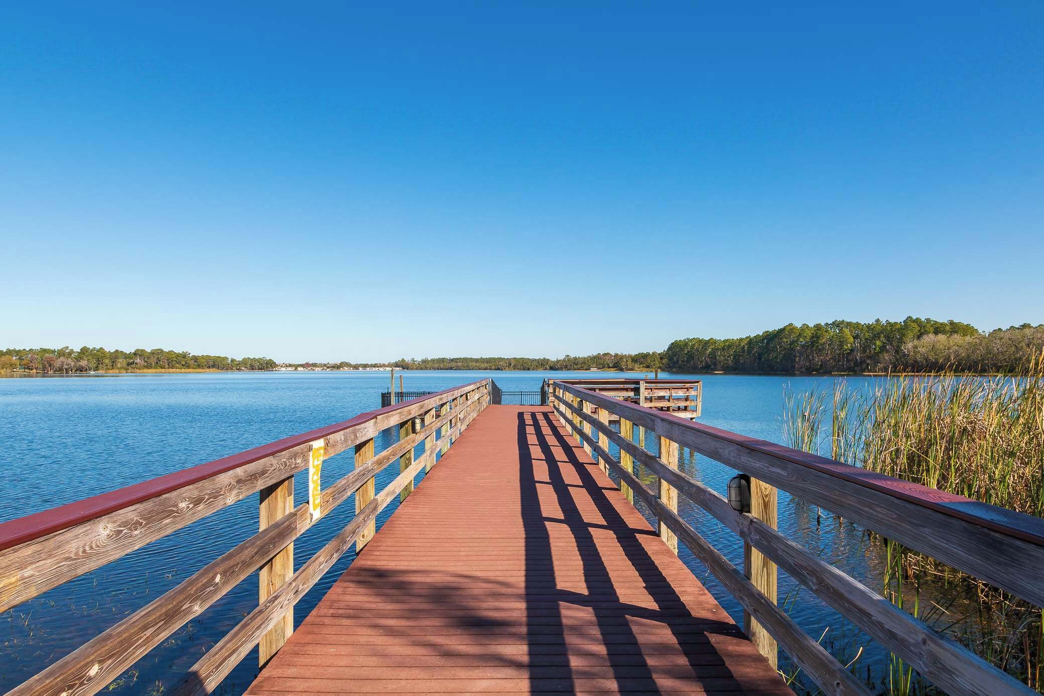 A wooden pier extending into a calm lake with clear skies.