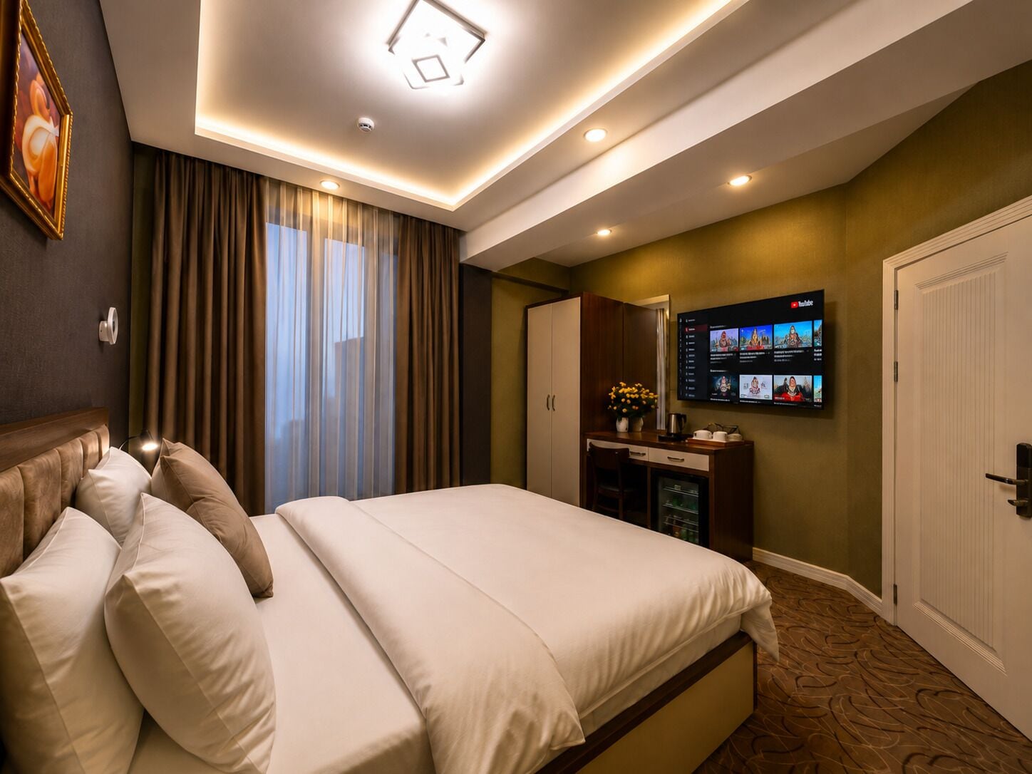 A hotel room with a bed, a desk with a flat-screen TV, curtains, and a door.