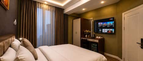 A hotel room with a bed, a desk with a flat-screen TV, curtains, and a door.