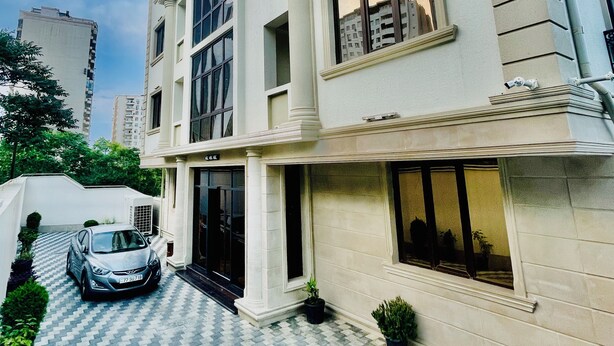 A multi-story building with a symmetrical facade, large windows, and a paved entrance area with potted plants.