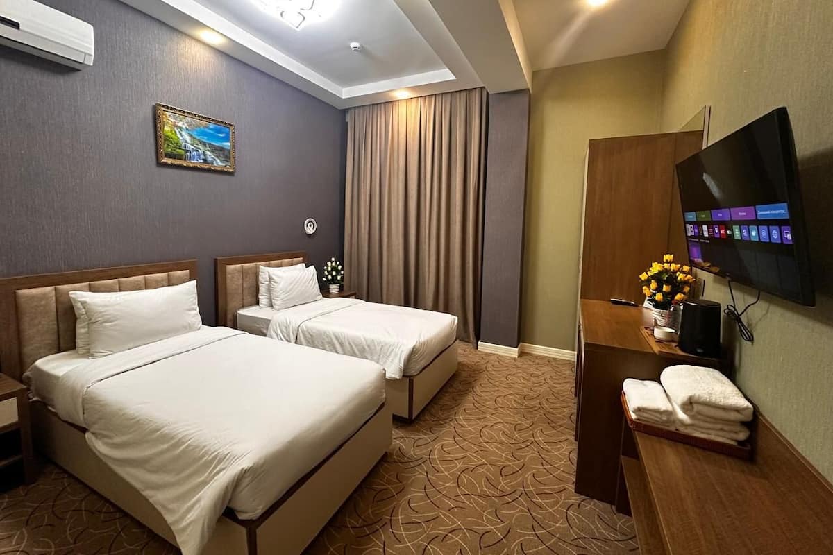 A hotel room with two beds, a TV, a desk with a computer, and a painting on the wall.