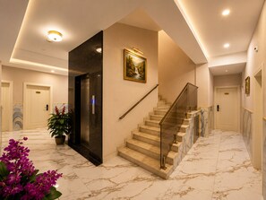 A hotel lobby with marble flooring, a staircase with glass railings, and a potted plant.