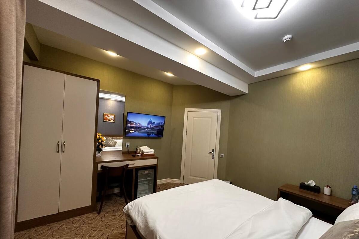 A hotel room with a bed, a desk with a TV, a wardrobe, and a door.